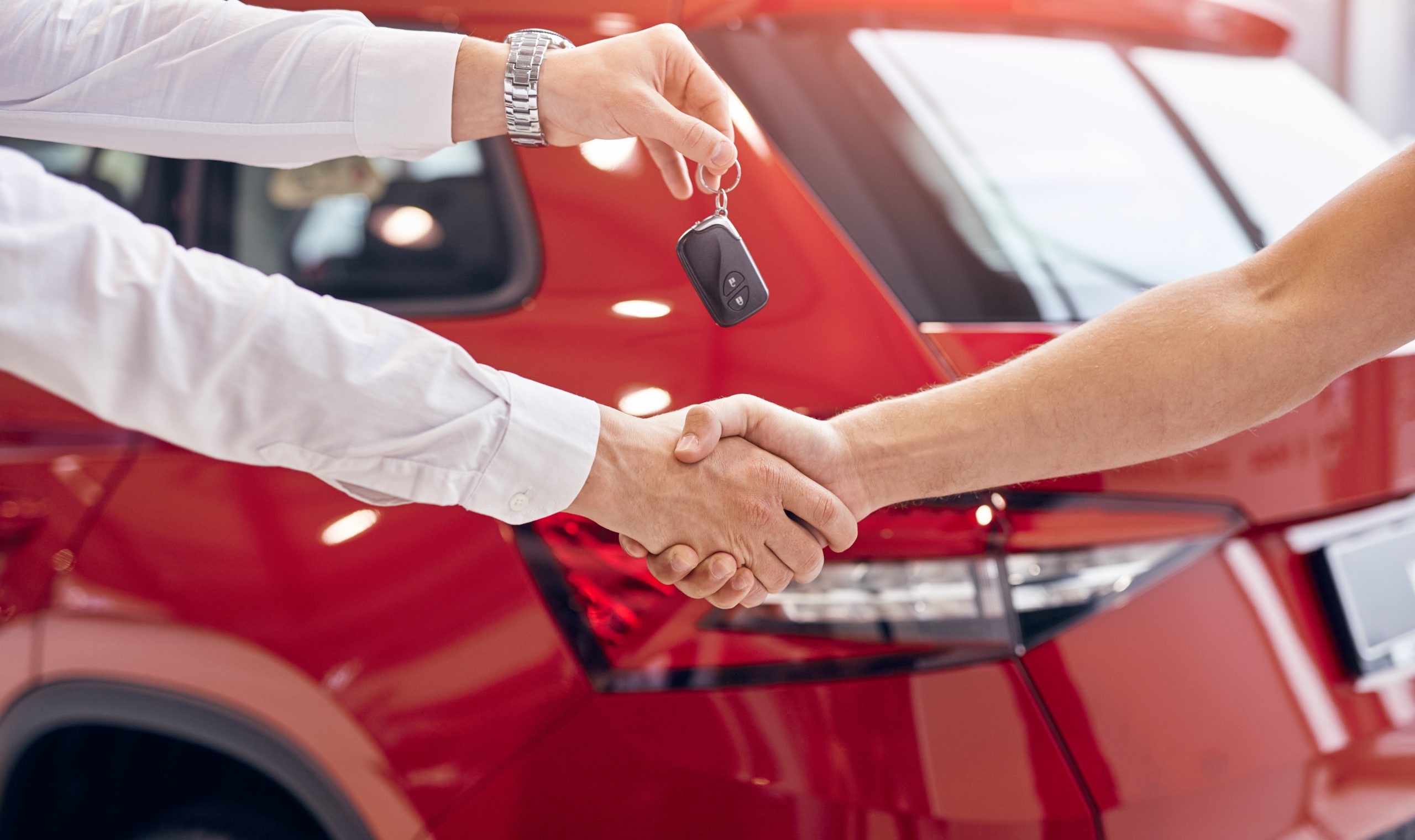 Handshake during a car purchase with keys exchanged beside a red vehicle.