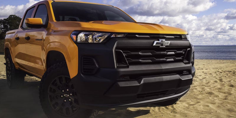 Orange Chevrolet pickup truck parked on a sandy beach with ocean backdrop.