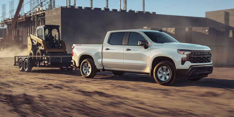 White Chevrolet Silverado 1500 towing a trailer on a dirt road