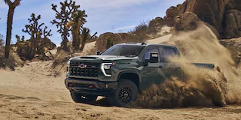 Green Chevrolet Silverado pickup truck driving through rugged desert terrain and kicking up dust.