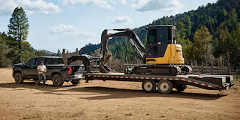 Chevrolet Silverado 2500 HD towing a trailer with heavy equipment at a worksite.