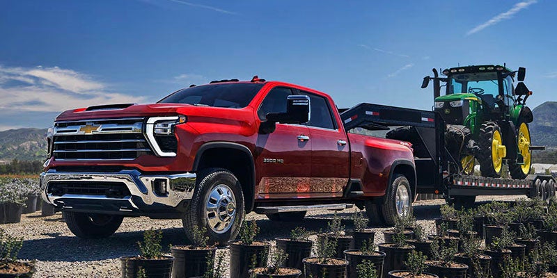 Red Chevrolet Silverado 2500 HD towing heavy equipment on a trailer.