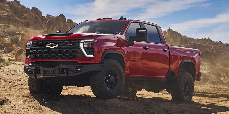 Red Chevrolet Silverado 2500 HD pickup truck parked on a rugged desert landscape.