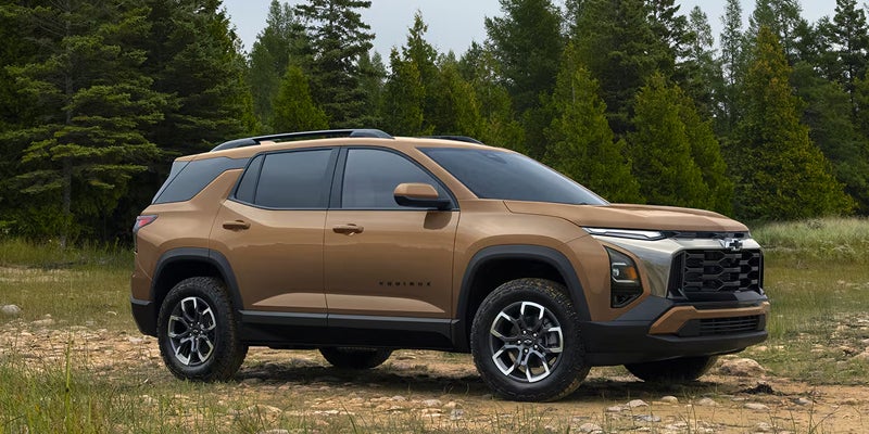 Brown Chevrolet Equinox SUV parked on a dirt path surrounded by trees.
