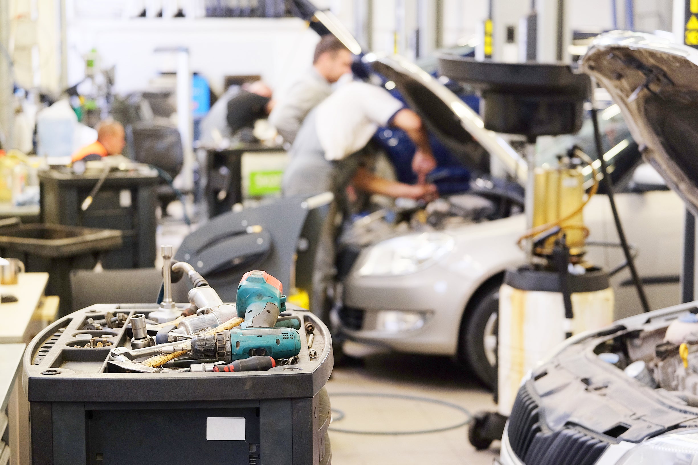 Automotive service technician working on a vehicle in a professional repair shop with tools in the foreground.
